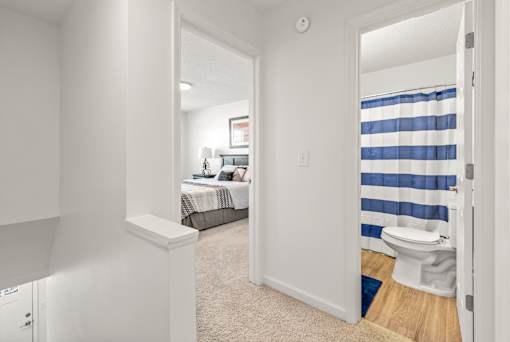 A white bedroom with a bed, toilet, and a window with blue curtains.