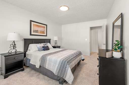 A bedroom with a bed, nightstand, and a plant on a dresser.