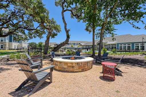 a fire pit with chairs and trees and a building in the background at Estraya Boerne, Boerne