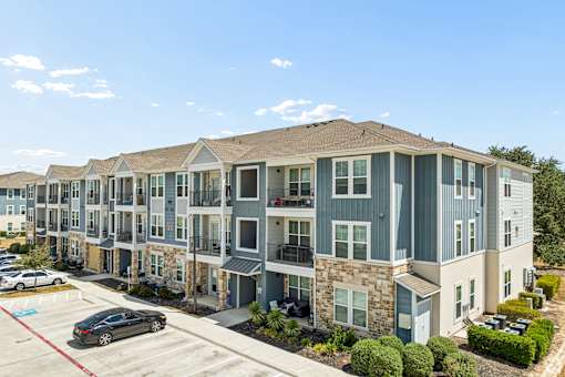 A row of modern apartment buildings with cars parked in front.