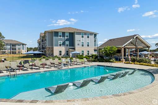 A swimming pool surrounded by lounge chairs and apartment buildings in the background.