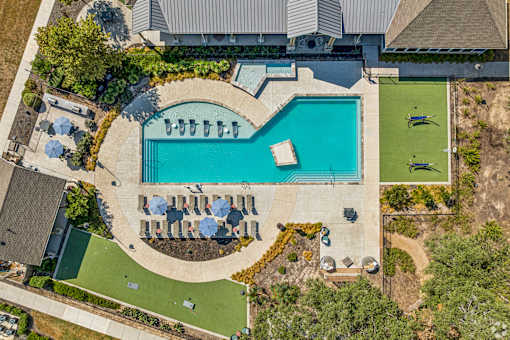 An aerial view of a swimming pool surrounded by a grassy area and a few trees.
