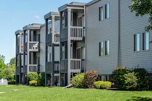 A grey apartment building with balconies and bushes in front.