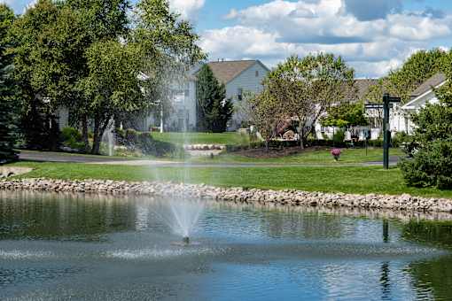 A fountain in the middle of a pond in a residential area.