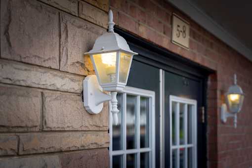 A white lamp is mounted on a brick wall next to a black door.