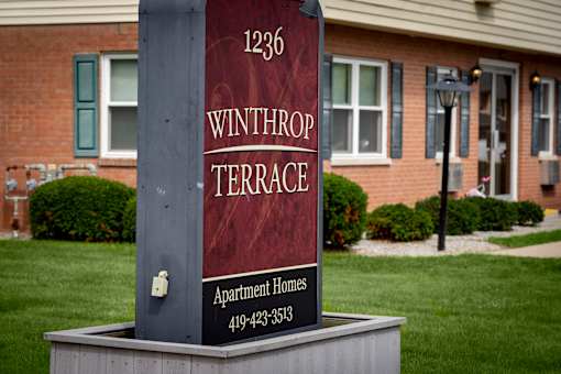 A sign for Winthrop Terrace Apartment Homes stands in front of a brick building.