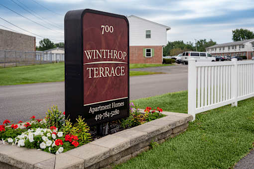 A sign for Winthrop Terrace Apartment Homes stands in front of a white fence.
