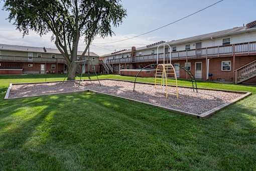 A playground with a yellow slide and a tree in the middle of a grassy area.