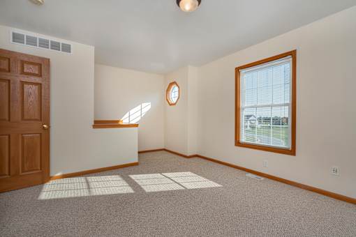 A room with a brown door, a window with blinds, and a round mirror on the wall.