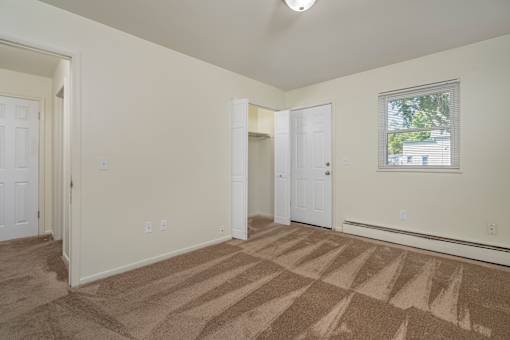 A room with carpeted floor and a window showing a tree outside.