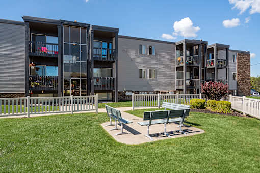 A modern apartment complex with a green lawn and benches in front.