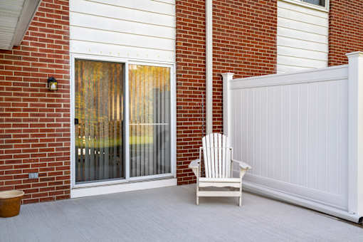 A white chair is placed in front of a white fence and a glass door.