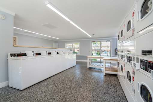 A laundromat with a row of washers and dryers on the right and a counter with a cash register on the left.