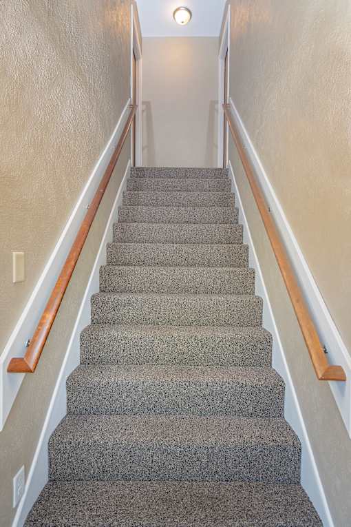 A staircase with a wooden handrail and grey carpeted steps.