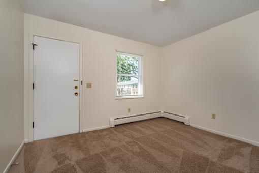 A room with a carpeted floor, a door, a window, and a wall-mounted air conditioner.