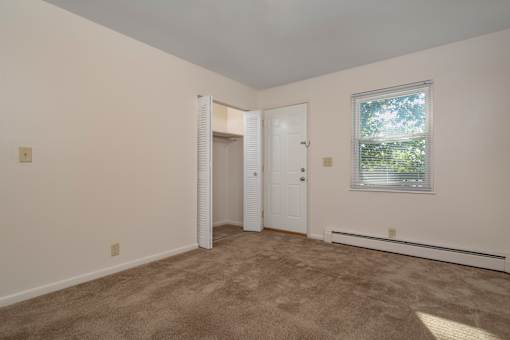 A room with a carpeted floor, a window with a view of trees, and a door leading to another room.