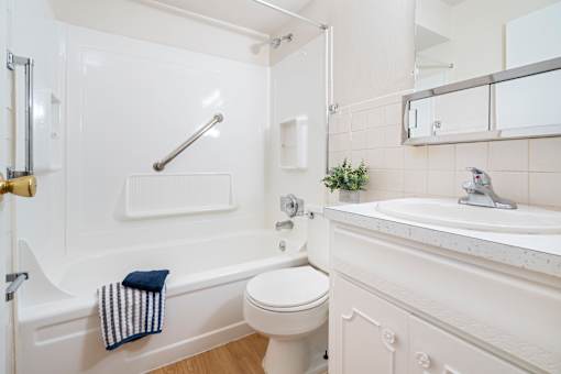 A white bathroom with a towel hanging on the tub.