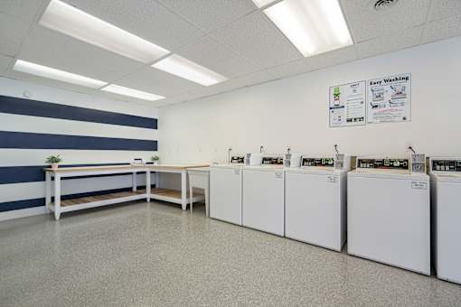 A laundry room with washers and dryers lined up on the wall.