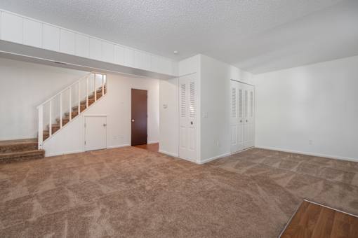 A large empty room with a staircase and a door.