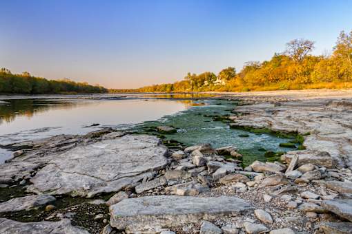 A rocky shoreline with a body of water and trees in the background.