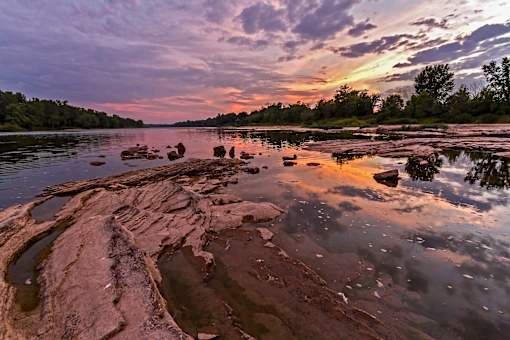 A serene landscape with a river, rocks, and a sunset.