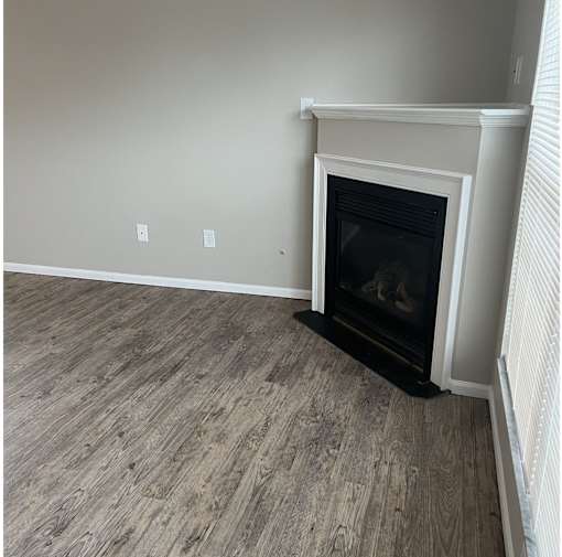 A fireplace with a white mantle and a black hearth sits in a room with wood flooring.