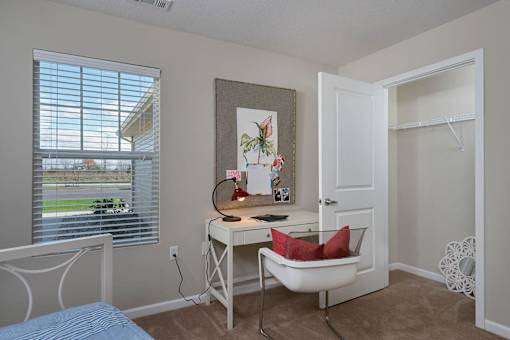 A room with a desk, chair, and a window with blinds.