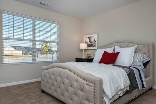 A bedroom with a large bed and a window with blinds.