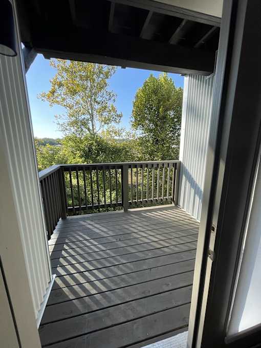 A view from inside a building looking up at a staircase leading to a balcony with trees in the background.