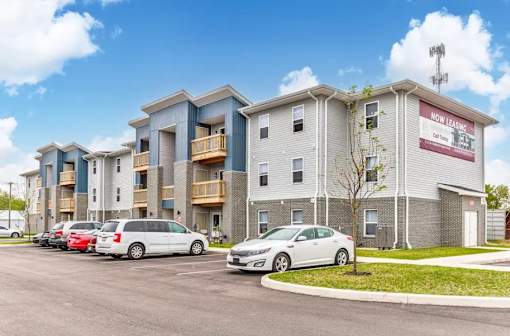 Apartment complex with cars parked in front and a sign that says "Now Leasing".
