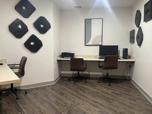 A room with a desk and chairs and a wall with artwork.
