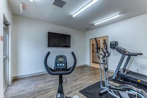 A home gym with a treadmill, exercise bike, and television.