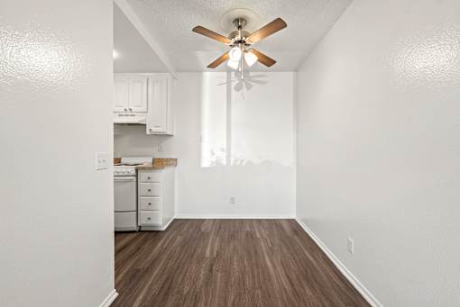 A white kitchen with a wood floor and a ceiling fan.