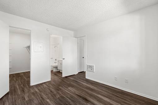 A white room with wood flooring and a doorway leading to another room.