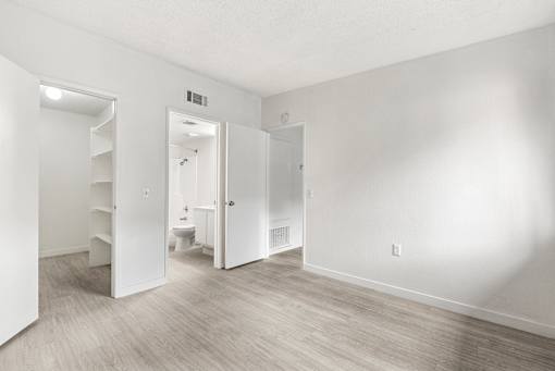A white room with a wooden floor and a toilet in the background.