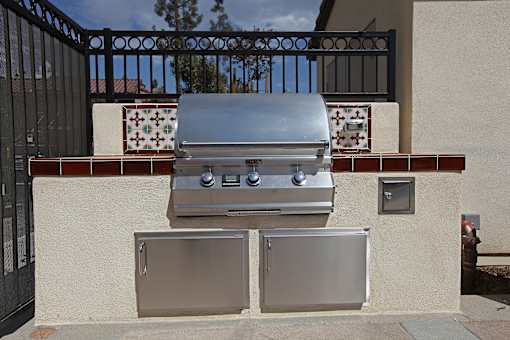 A silver grill is on top of a wall next to a wall-mounted fridge.