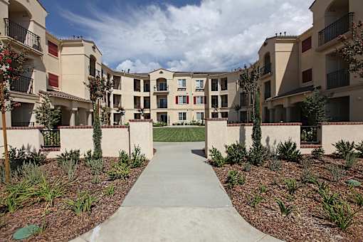 A concrete walkway leads through a landscaped courtyard between two rows of apartment buildings.