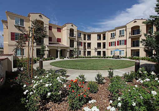 A large building with a courtyard surrounded by trees and flowers.