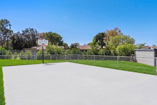 A basketball court surrounded by a fence with houses and trees in the background.