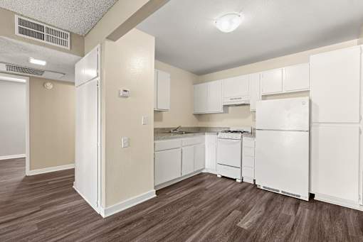 A kitchen with white appliances and brown flooring.
