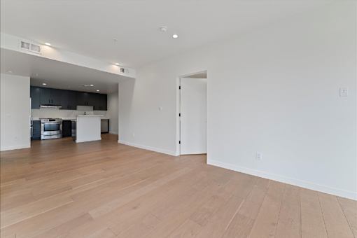 A large empty room with wooden floors and a kitchen area in the background.