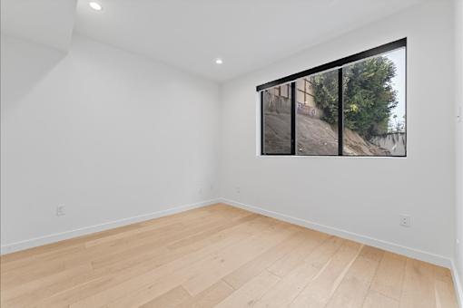 Empty room with wooden flooring and a large window.