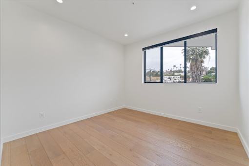 Empty room with wooden floor and a window showing a view of trees and a building.