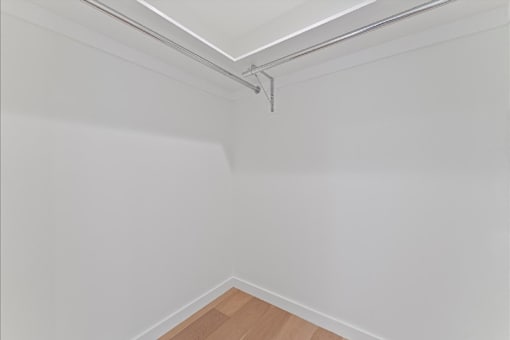 A white wall with a wooden floor and a metal pipe on the ceiling.