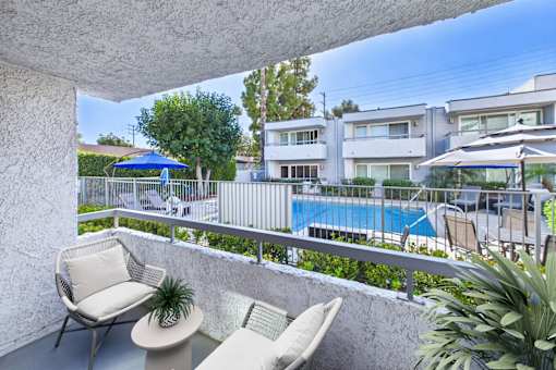 A balcony with a chair and a table overlooking a pool.