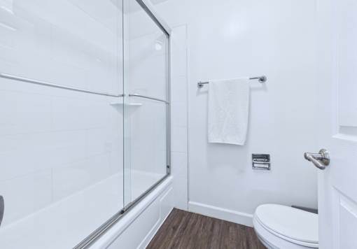 A white bathroom with a glass shower door and a towel hanging on the towel rack.