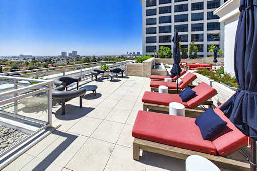 A patio with red cushioned seating and blue umbrellas overlooking a city skyline.
