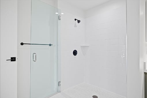A white bathroom with a glass shower door and a drain in the floor.