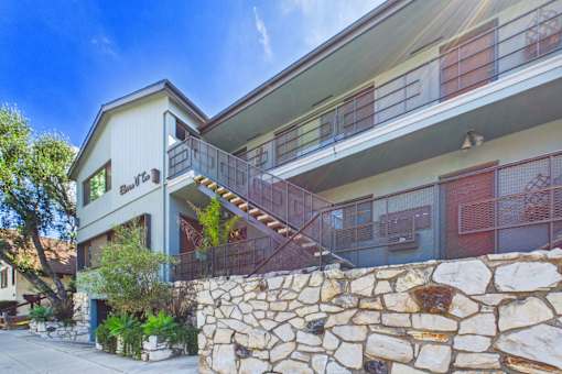 A stone wall separates a house from a building with balconies.