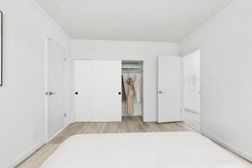 A room with a white bed and a wardrobe with a dress hanging in the doorway.